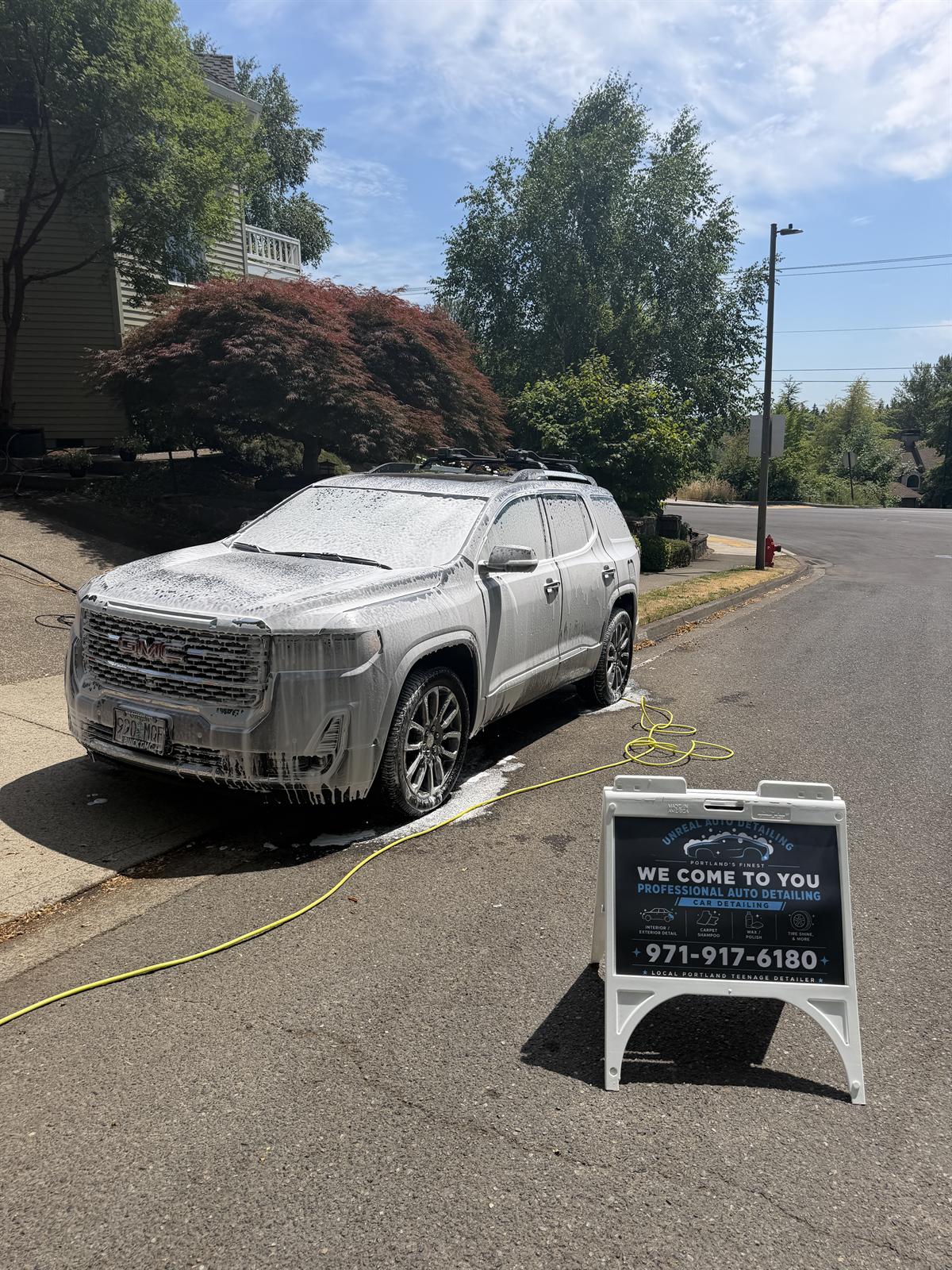 GMC covered in foam curbside next to the Unreal Auto Detailing sign
